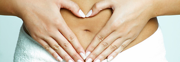 Dekoratives Bild mit zwei Händen, welche ein Herz über dem Bauch einer Person formen, die ein weißes Handtuch trägt.